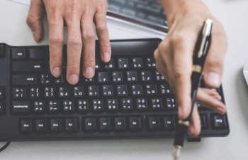 a hand holding a pen above a computer keyboard